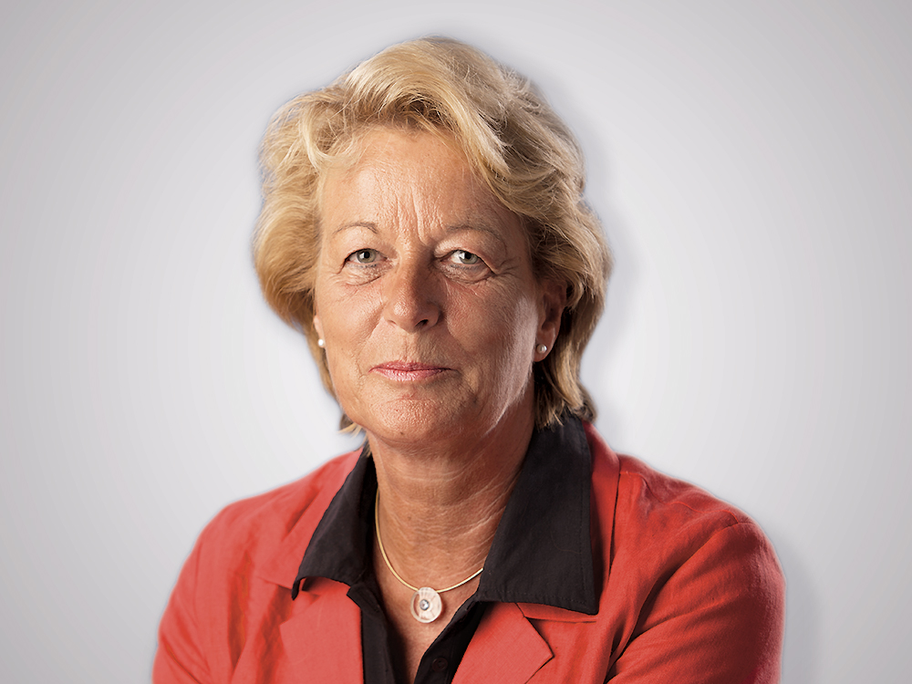 Portrait einer Frau mit blonden Haaren, die einen roten Blazer und eine schwarze Bluse trägt.