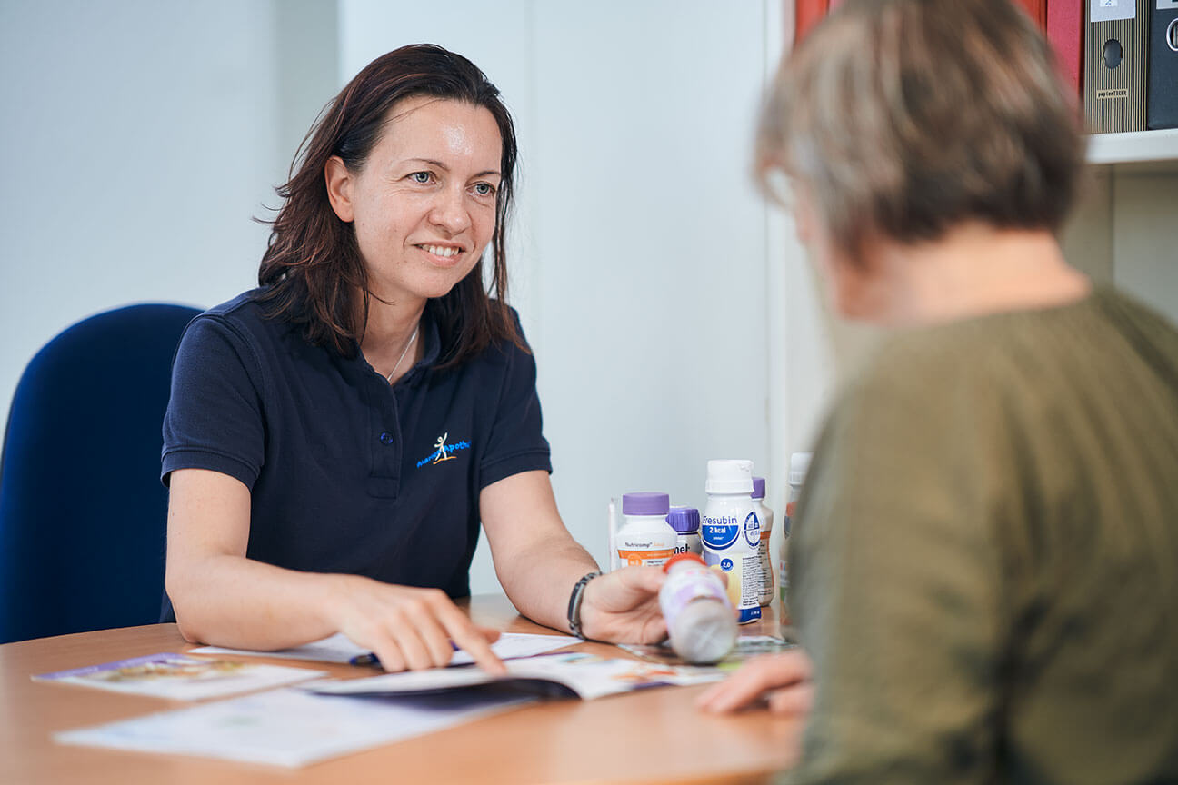 Eine Frau berät eine ältere Person am Tisch über Gesundheitsprodukte.