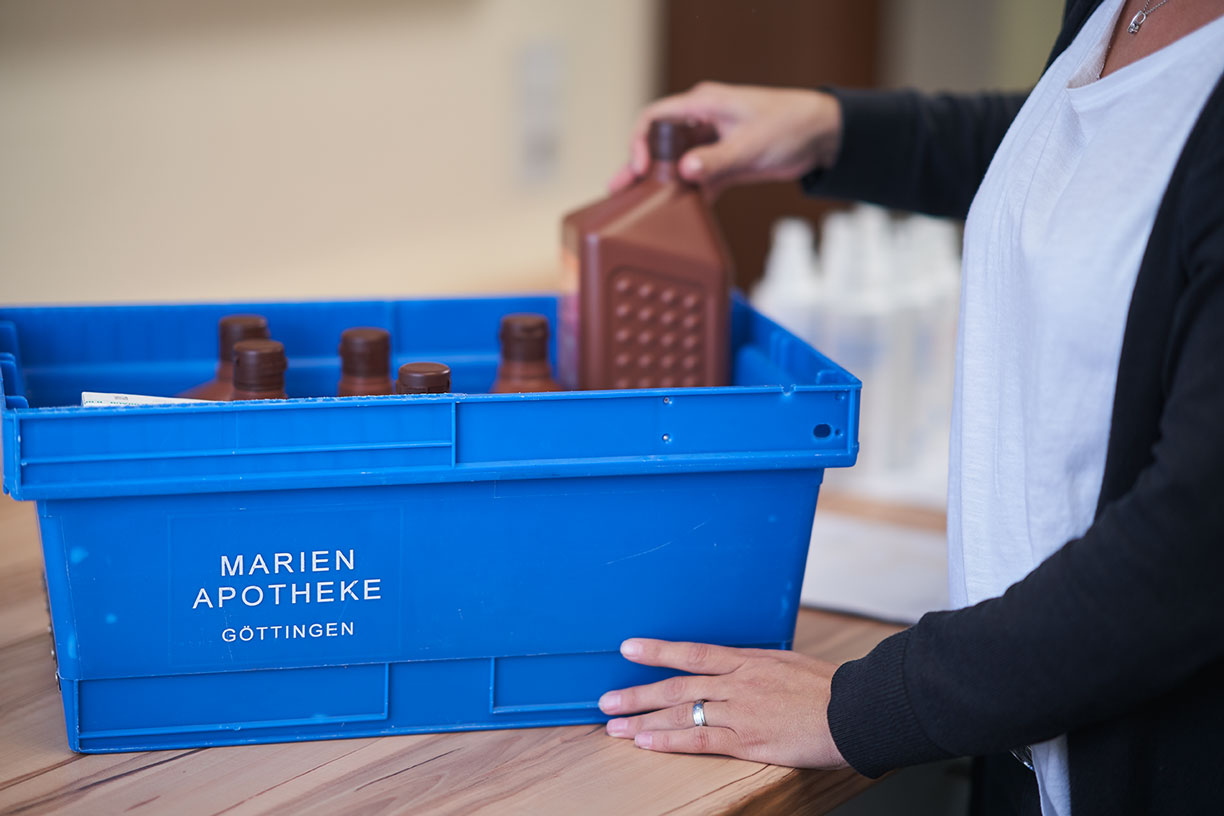 Blaue Box mit Flaschen, beschriftet mit Marien Apotheke Göttingen, auf einem Tisch.