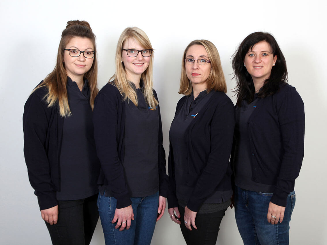 Vier Frauen in Pullovern posieren vor einem neutralen Hintergrund.