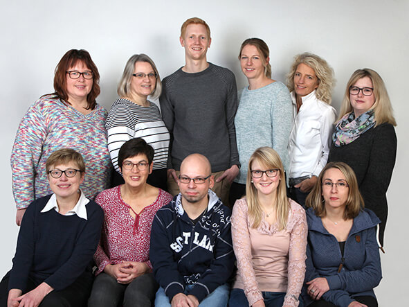 Gruppenportrait von zehn Personen vor einem neutralen Hintergrund.
